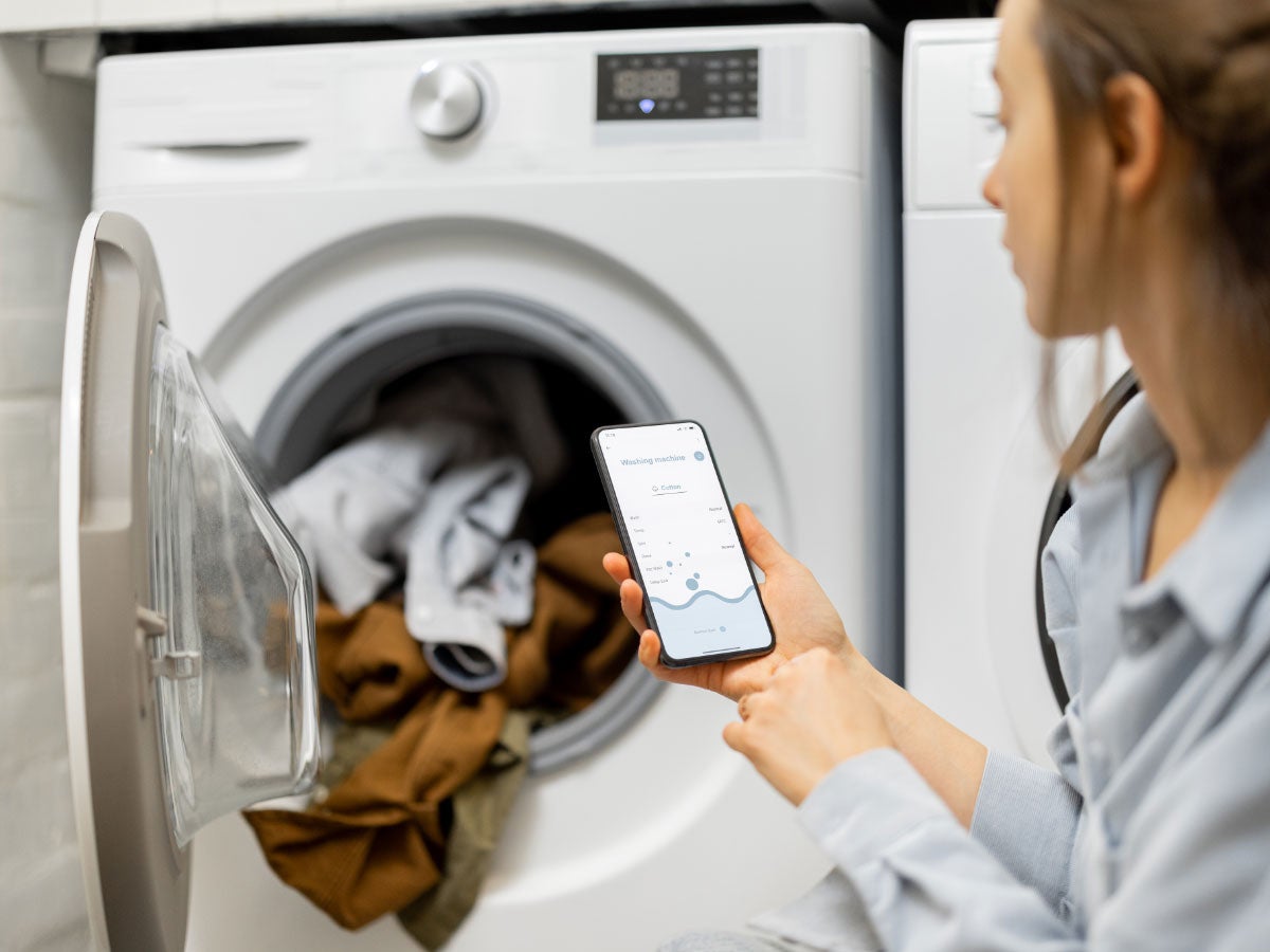 Person looking at a washing machine app while doing laundry